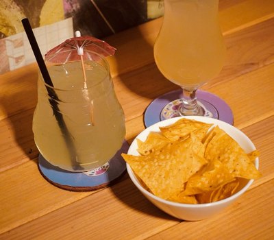 Dois drinks e uma tigela de nachos sobre a mesa de madeira.