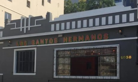 A fachada cinza da casa de dia, com o nome pintado em verde e vermelho e o número 1058.