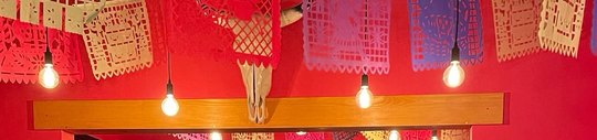 Bandeirinhas de papel picado penduradas no teto do salão, sobre a parede vermelha.