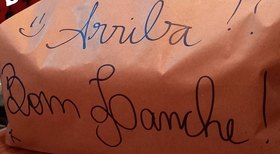 Sacola de entrega com “Arriba!! Bom Panche!” escrito à mão.