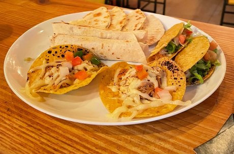 Prato com tacos, tortilhas e uma tostada, servido na nossa mesa de madeira.